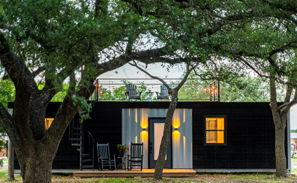 Een zwarte containerwoning met de lampen aan