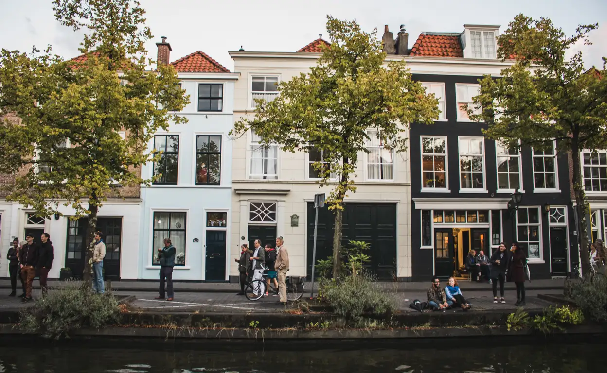 Aangezicht van huizen aan de overkant van een gracht met bomen voor het huis die blad hebben.