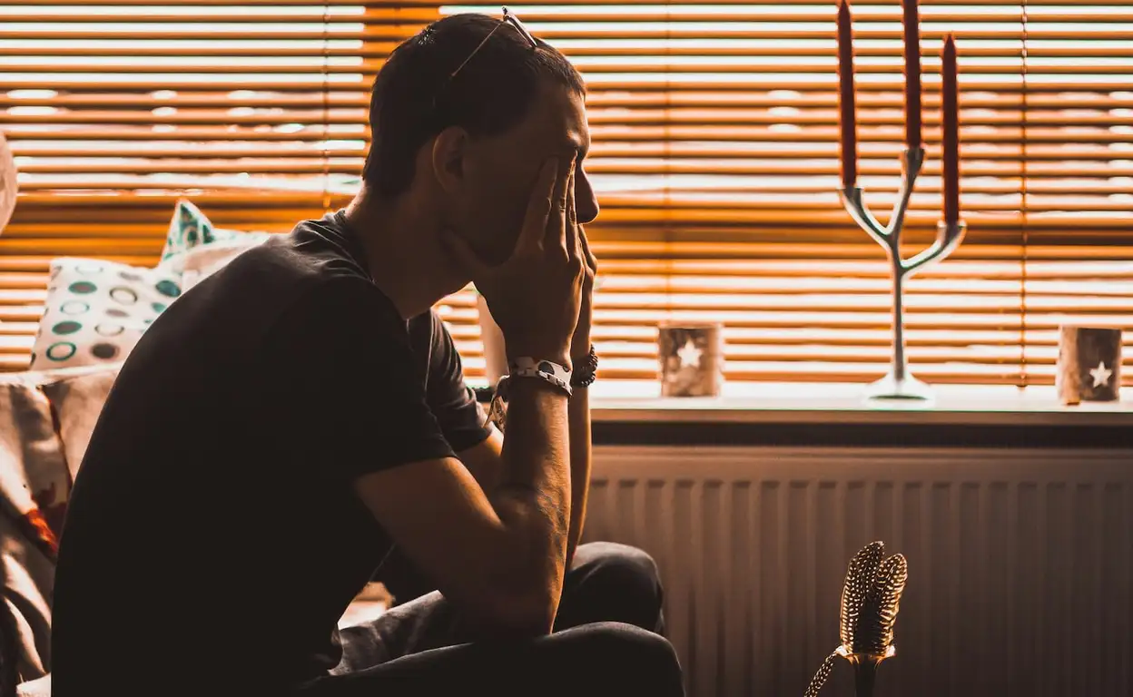 Een jonge man zit in gedachten verzonken voor een raam