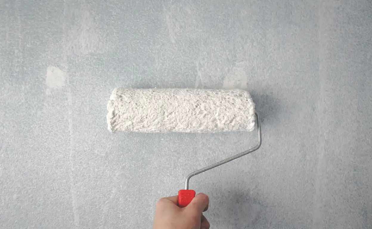 Iemand verft de muur met een verfroller met witte verf