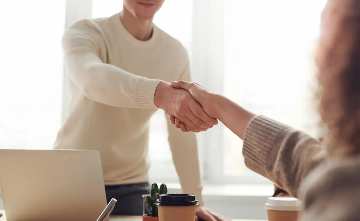 Een man geeft iemand de hand. Op tafel staan kopjes koffie