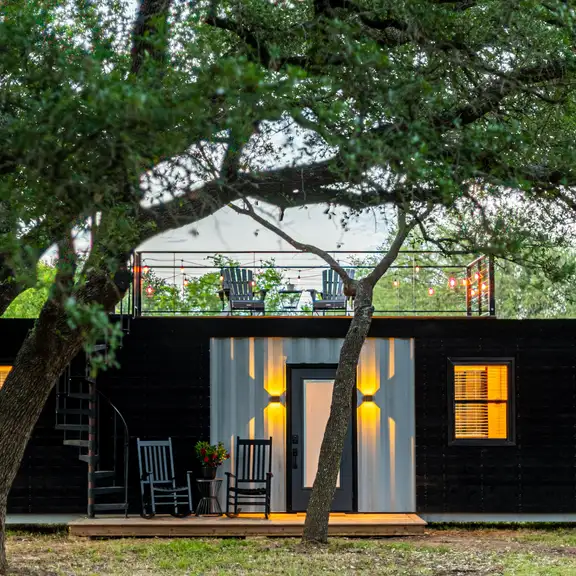 Een zwarte containerwoning met de lampen aan