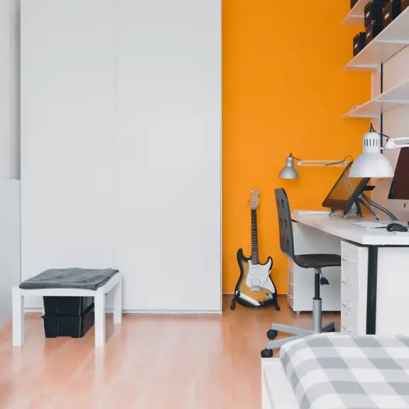 Een studentenkamer met een oranje muur en een gitaar tegen de muur