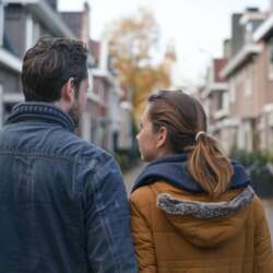 Een man en een vrouw lopen in een straat met huurwoningen