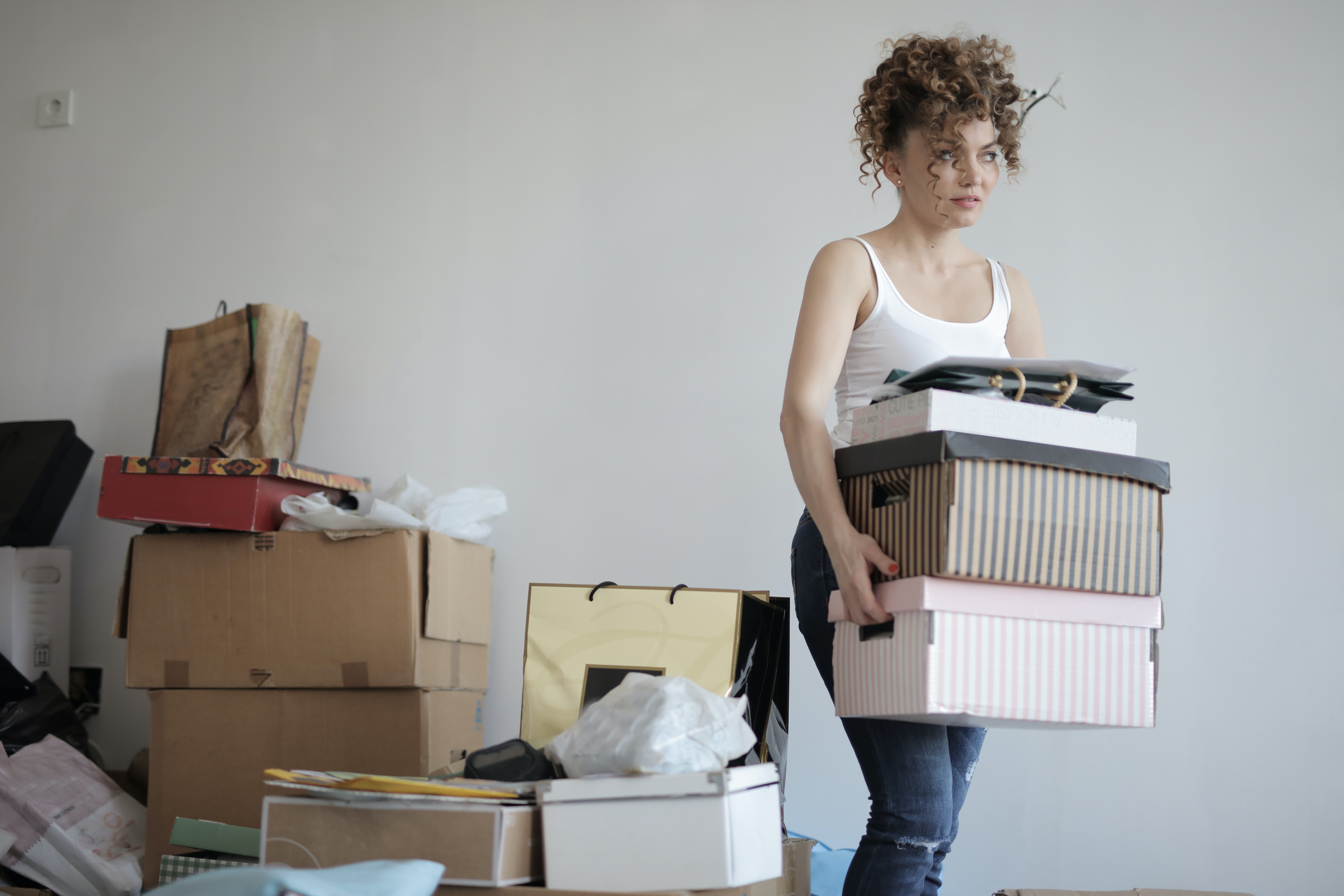 Een verhuizende jonge vrouw draagt een doos. Er staan dozen in allerlei formaten op de achtergrond.